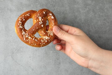 Woman with tasty pretzel near grey textured wall, closeup