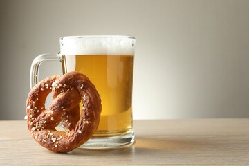 Tasty pretzel and glass of beer on wooden table against grey background, closeup. Space for text