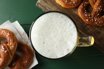 Tasty pretzels and glass of beer on green wooden table, flat lay
