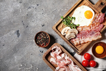 Board with fried eggs, bacon, mushroom and tomatoes on grey grunge background