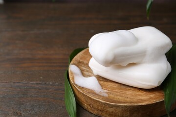 Soap bars with foam on wooden table, closeup. Space for text