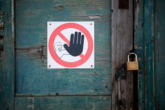 Weathered wooden door with peeling turquoise paint. Affixed is a caution sign: a black hand symbol inside a red circle with a diagonal line, indicating prohibition. 