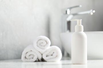 Liquid soap in bottle and towels on white textured table in bathroom, selective focus. Space for text