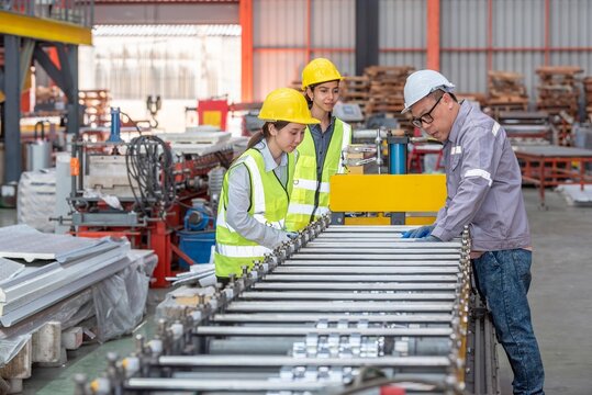 Industrial manufactu workers in safety gear inspecting conveyor belt with machinery and equipment in large factory warehouse setting