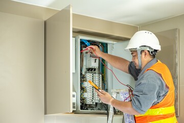 Professional electrician in safety helmet and reflective vest inspecting an electrical panel troubleshooting and performing maintenance for electrical systems