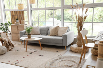 Stylish interior of living room with soft sofa, window, coffee table and armchair
