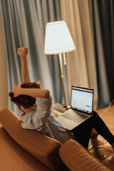 Woman stretches arms while working on laptop from couch symbolizing stretching at home office digital detox and remote work wellness showing importance of healthy posture habits and mindful pauses