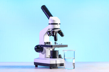 Modern microscope and laboratory flask with liquid on white table