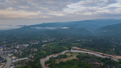 A stunning aerial view of a winding river flowing through a vast rural landscape at dawn. The soft morning light and misty atmosphere create a tranquil and picturesque scene, with scattered villages