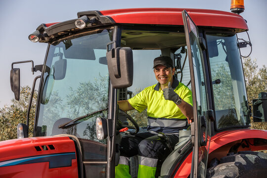 Smiling farmer in bright attire driving a tractor in an olive grove