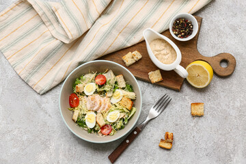 Bowl with tasty chicken Caesar salad, peppercorn and gravy boat of sauce on grey background