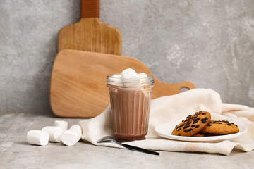 Glass of sweet chocolate milk with marshmallows and tasty cookies on grey background