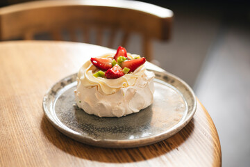 Pavlova cake with whipped mascarpone cream and fresh strawberry slices in cafe.