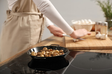Woman and frying pan with roasted mushrooms on electric stove in kitchen