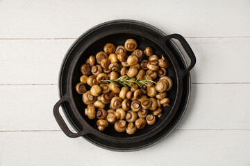 Frying pan with roasted mushrooms and rosemary on white wooden background