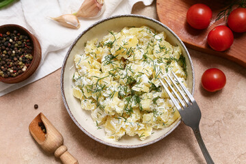Bowl of tasty potato salad with dill, tomatoes, peppercorns and garlic on beige grunge background