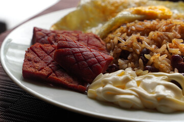 Close-up of a gallo pinto, a typical Costa Rican dish with rice, red beans, sausage, cream, and a fried egg.