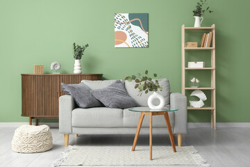 Sofa, pouf, table and vase with eucalyptus branches in interior of living room