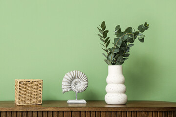 Statuette and vase with eucalyptus branches on chest of drawers near green wall in room, closeup © Pixel-Shot