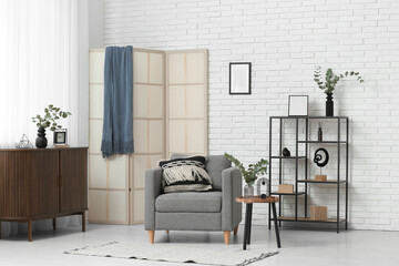Interior of stylish room with grey armchair and beautiful eucalyptus branches on coffee table