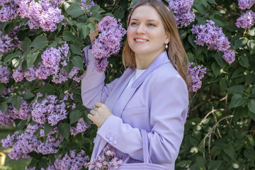 A beautiful young blonde woman, against a background of blooming lilacs, in a lilac trouser suit....