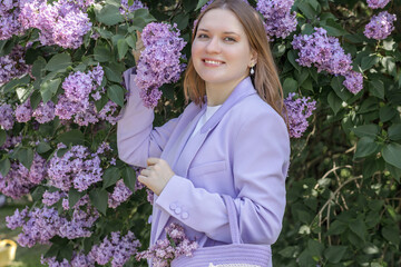 A beautiful young blonde woman, against a background of blooming lilacs, in a lilac trouser suit....