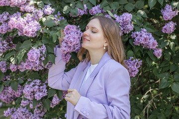 A beautiful young blonde woman, against a background of blooming lilacs, in a lilac trouser suit....
