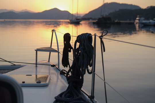 scenic view of morning calm tranquil sunrise from the boat deck at anchor stop, rising sun, mountains, sea with light reflections, twilight colors, sailing boats, serene harbour