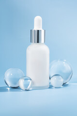 Mockup of glass dropper bottle with face serum or essential oil on blue background with glass balls. The concept of beauty cosmetics, natural products for moisturizing and restoring the skin.
