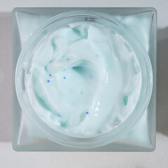 top view of frosted glass jar with collagen face cream. Skincare concept on blue background with strong shadows. Natural cosmetic concept for face body care.