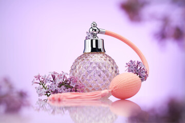 Bottle of perfume and lilac flowers on mirror surface against violet gradient background, selective...