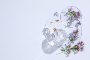 Bottle of perfume and beautiful lilac flowers on white background, flat lay. Space for text