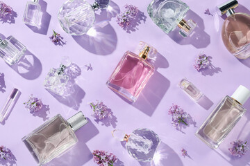 Luxury perfumes and beautiful lilac flowers on light violet background, flat lay