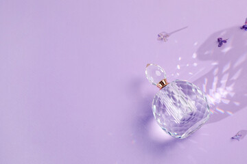Bottle of perfume and beautiful lilac flowers on light violet background, flat lay. Space for text