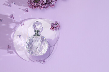 Bottle of perfume and beautiful lilac flowers on light violet background, flat lay. Space for text