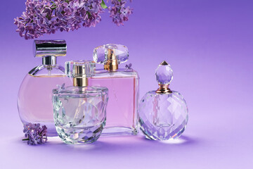 Bottles with perfumes and lilac flowers on purple gradient background, closeup