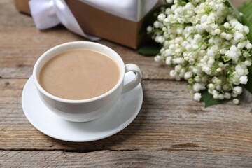 Bouquet of beautiful lily-of-the-valley flowers, coffee and gift on wooden background, closeup