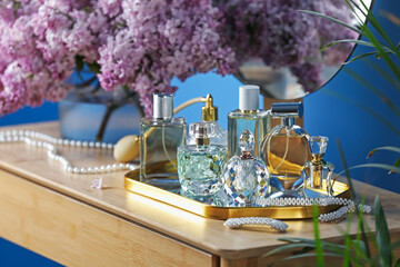 Bottles with perfumes, lilac flowers and accessories on dressing table indoors