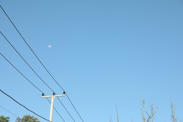 Electricity pole and wires against blue sky with moon, low angle view