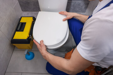 Plakat Professional plumber repairing toilet bowl in restroom, closeup