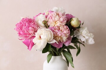 Bouquet of beautiful peonies in vase against beige wall indoors, closeup