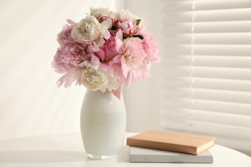 Bouquet of beautiful peonies in vase and books on white table indoors. Space for text
