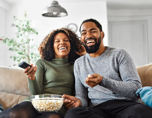 Portrait of a happy young couple watching tv together at home. Shot of a couple resting on the couch watching television