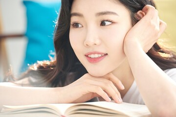 Fototapeta premium Tired Young Female Student Resting Head on Open Book at Desk in Bright Living Room