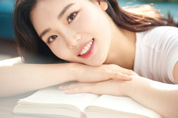 Obraz premium Tired Young Female Student Resting Head on Open Book at Desk in Bright Living Room