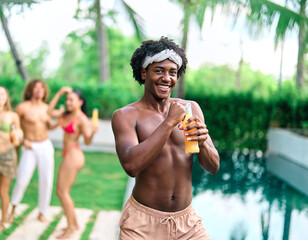 Naklejka premium Young people having fun dancing and drinking and bonding listening to music at a party by pool in a villa or resort, Young man enjoying vacation in a tropical resort hotel