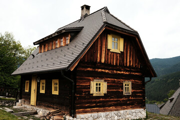Traditional log house in Drvengrad village, Serbia, with yellow wooden windows and a stone foundation.