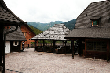 Courtyard of wooden buildings with gazebo and mountains in the background in Drvengrad, Serbia.