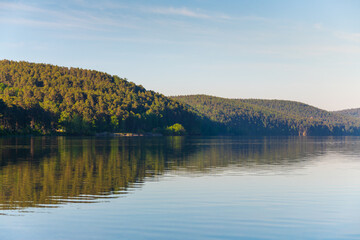 Beautiful lake with clear blue water at sunrise. Mountains are reflected in the calm water surface. Turgoyak lake in Southern Urals, Russia.