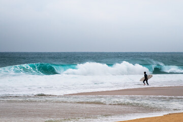 Atlantic ocean coast in Nazare, Portugal. Surfer with surfboard on the beach